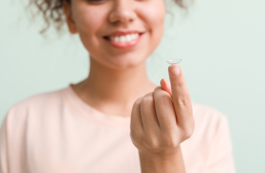 A smiling young woman holds a contact lens on her left index finger.