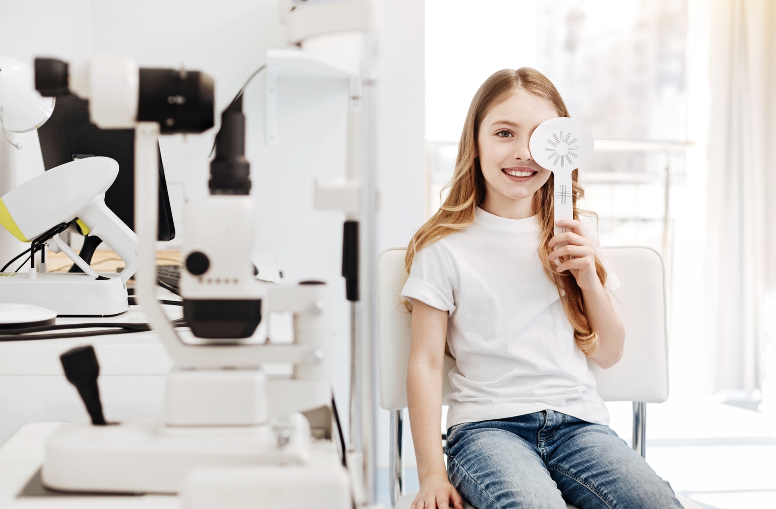 Young smiling girls in a chair at the optometrist's office as she uses an occluder.