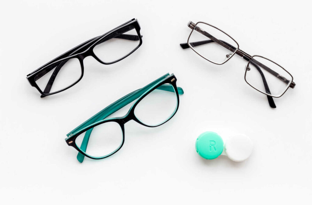 Three pairs of glasses and a contact lens case resting on a white background.