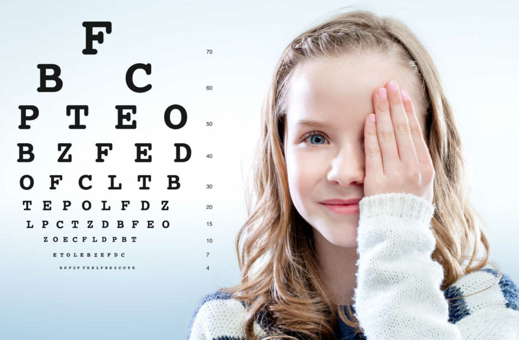 A girl in a blue and white colored sweatshirt is covering her left eye on her left hand for a Snellen chart exam.