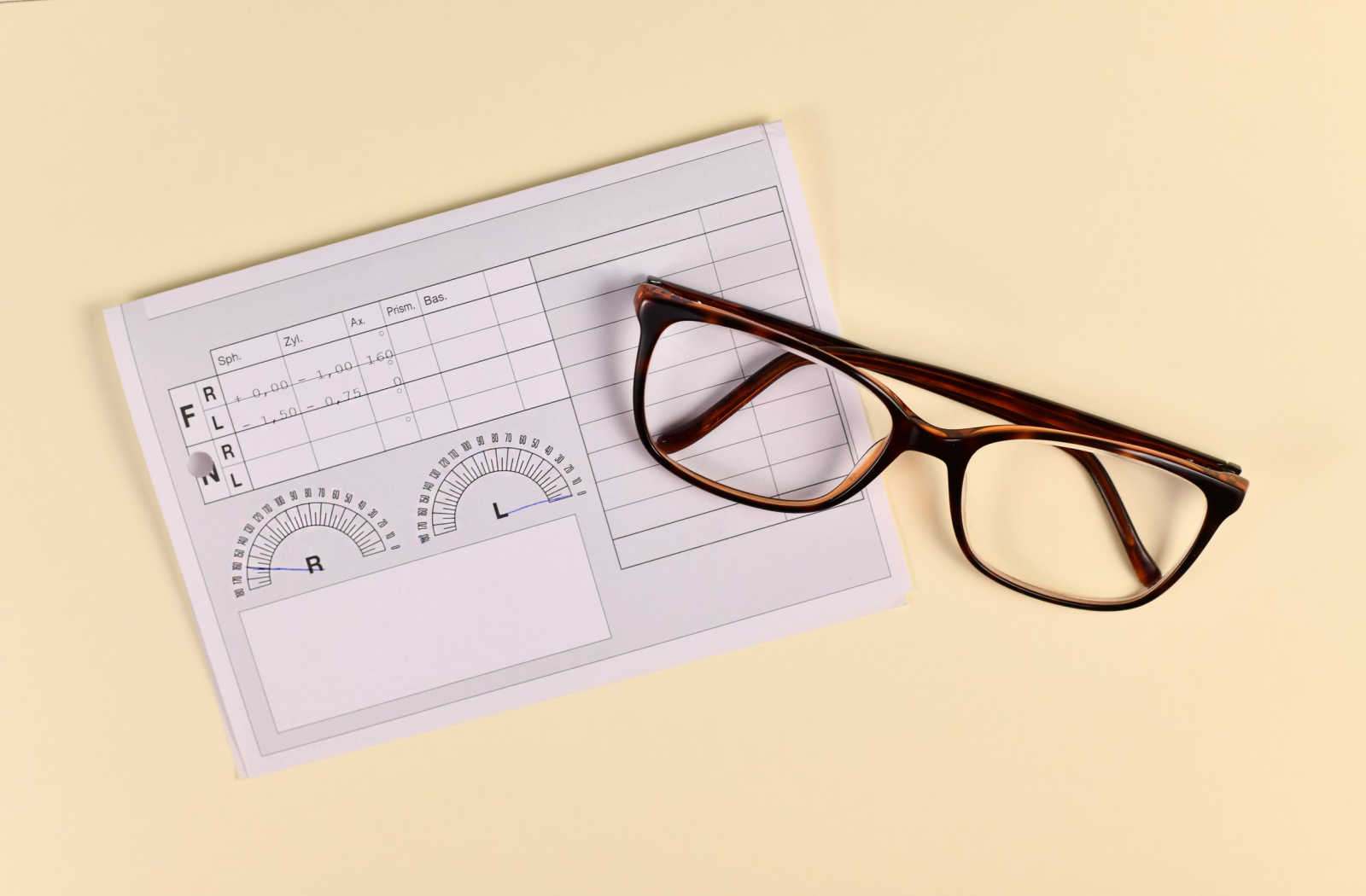 Pair of glasses and a prescription lens sheet on a yellow background.