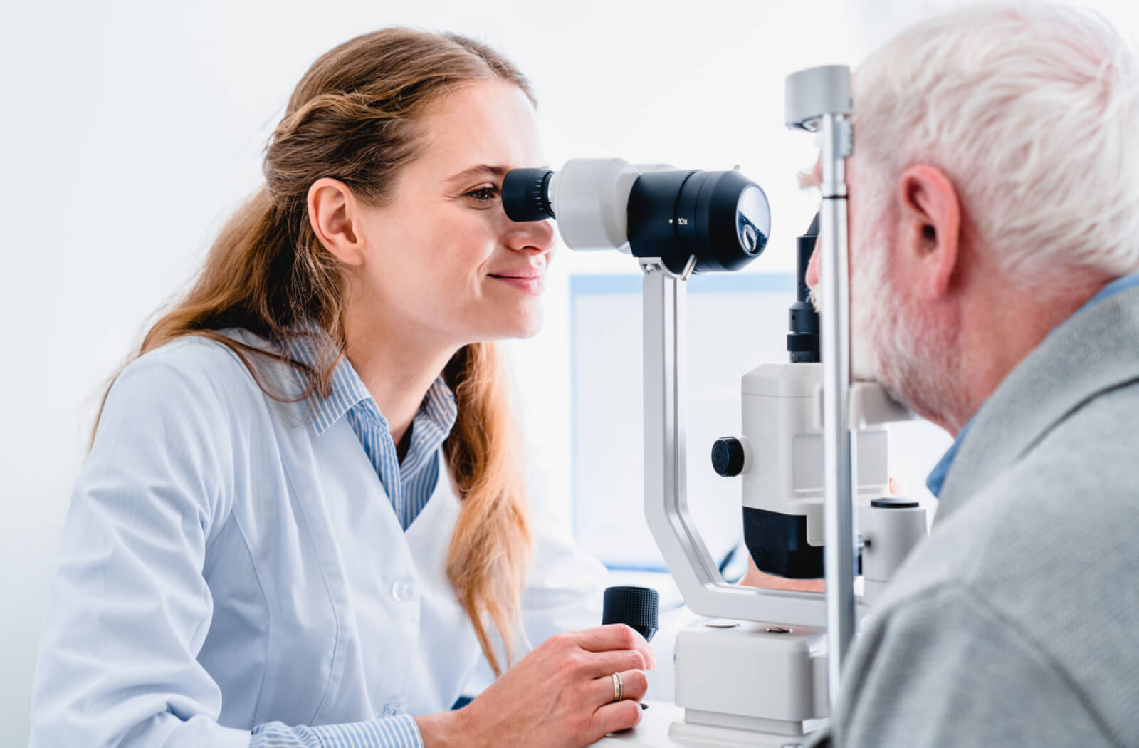 A close-up of a  female optometrist looking into a medical device to perform an eye exam on a senior man.