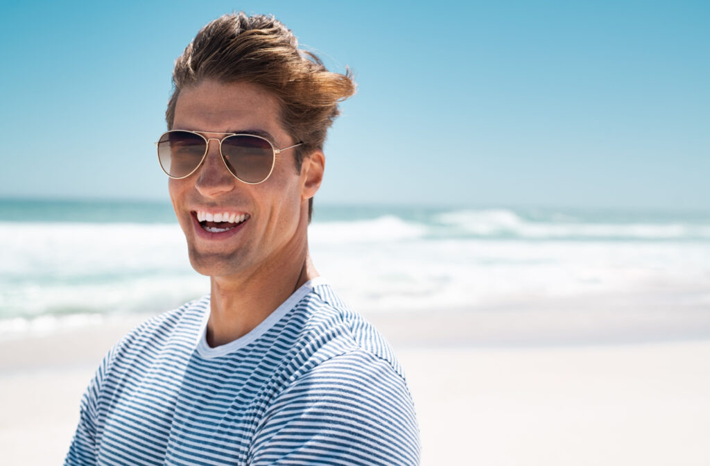 Close-up of a man on a beach smiling and wearing dark sunglasses.