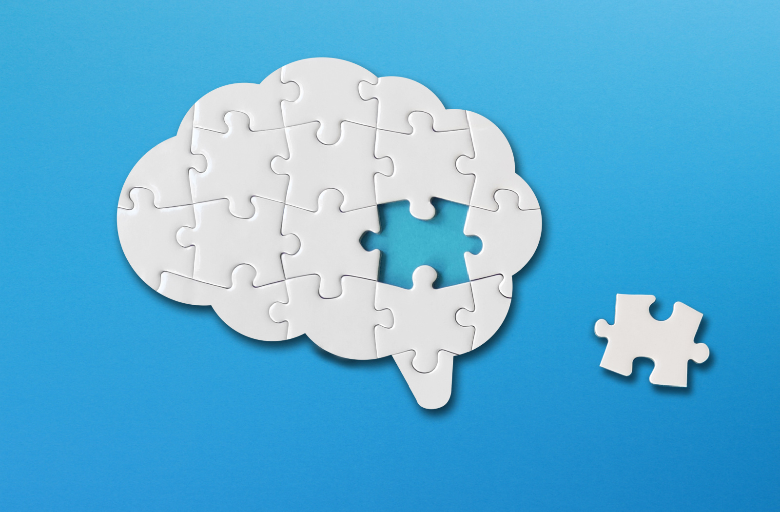 Brain assembled out of white puzzle pieces against a blue background.