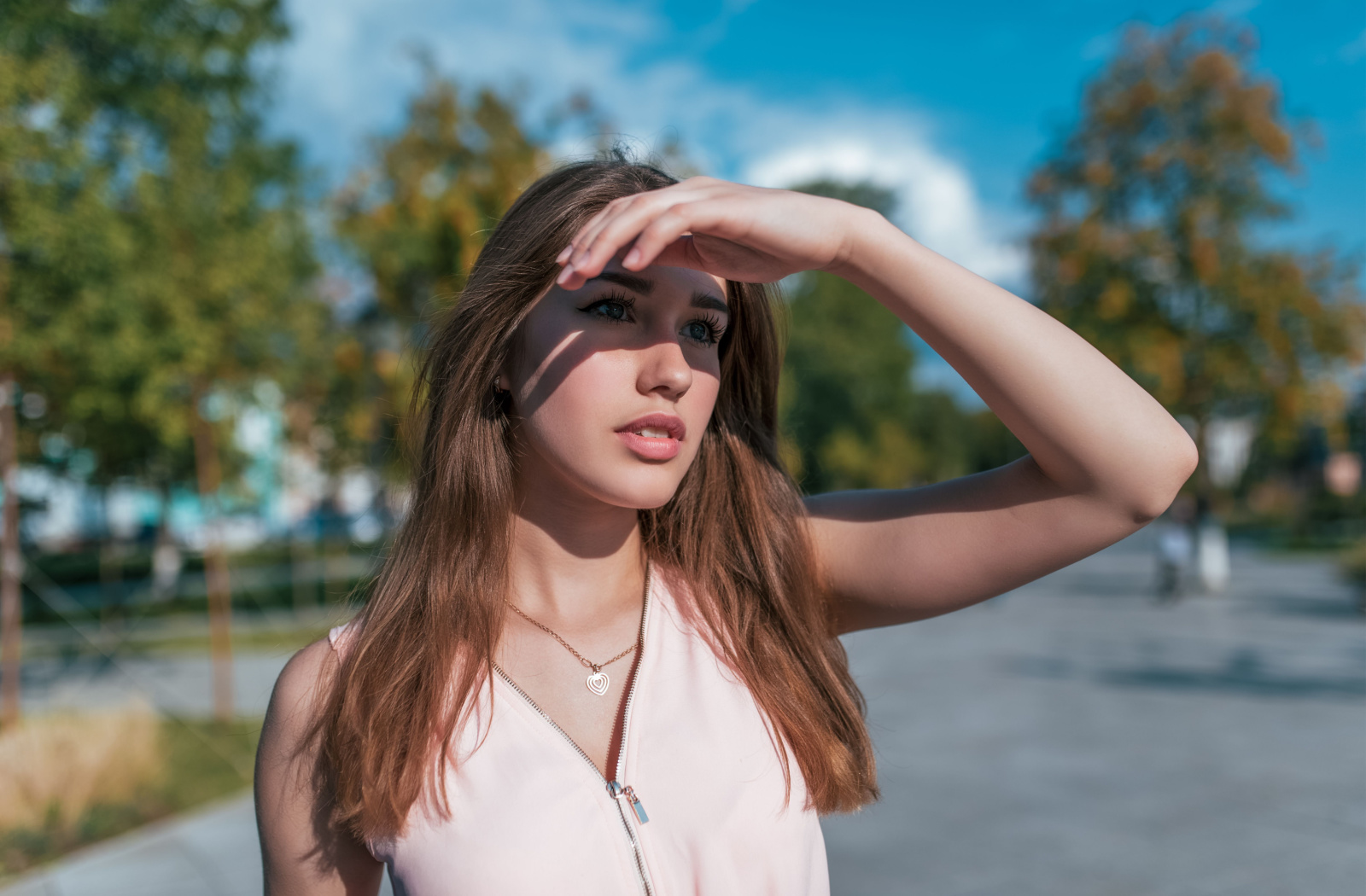 Girl outside putting her hand above her eyes to cover them from the sun.