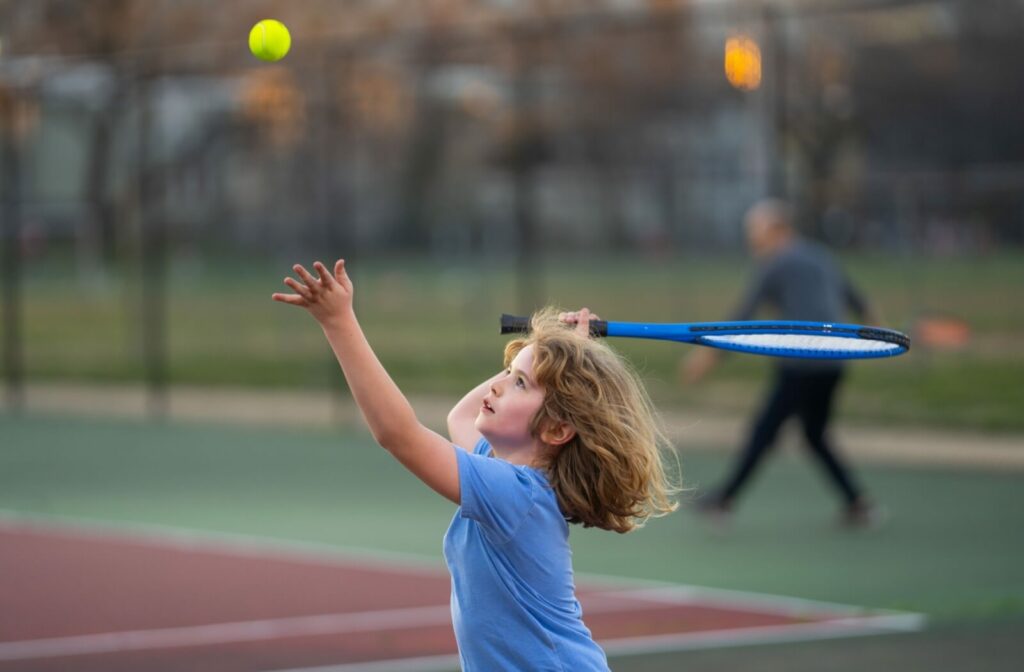 A child throwing a tennis ball in the air and using depth perception to decide when to hit it with their racket.